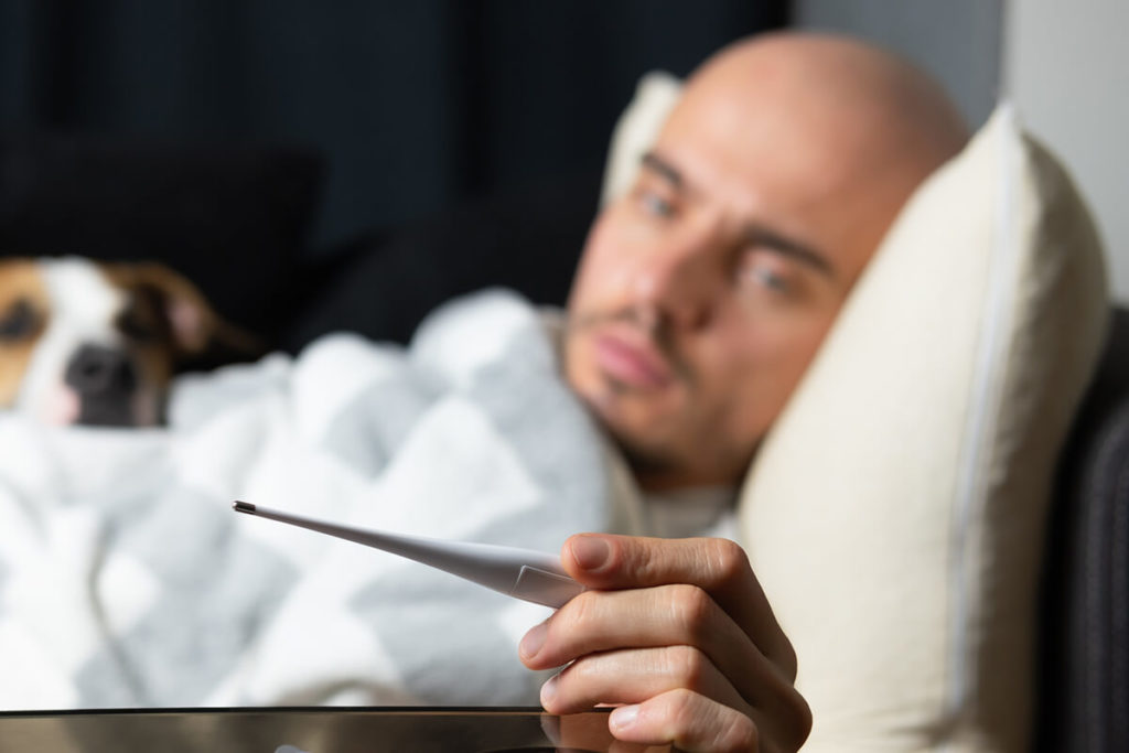 Man sick on a couch taking temperature