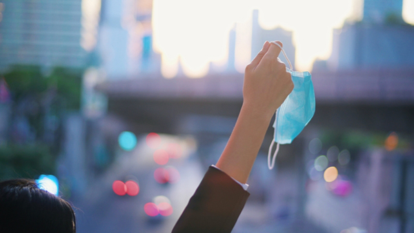 Woman holding up mask while on streets of city