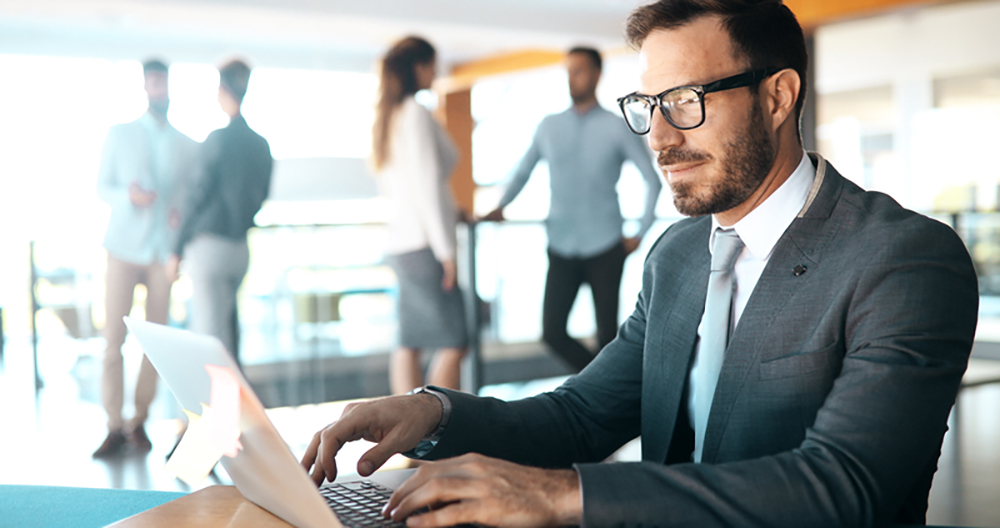 man working in open office with colleagues talking in background