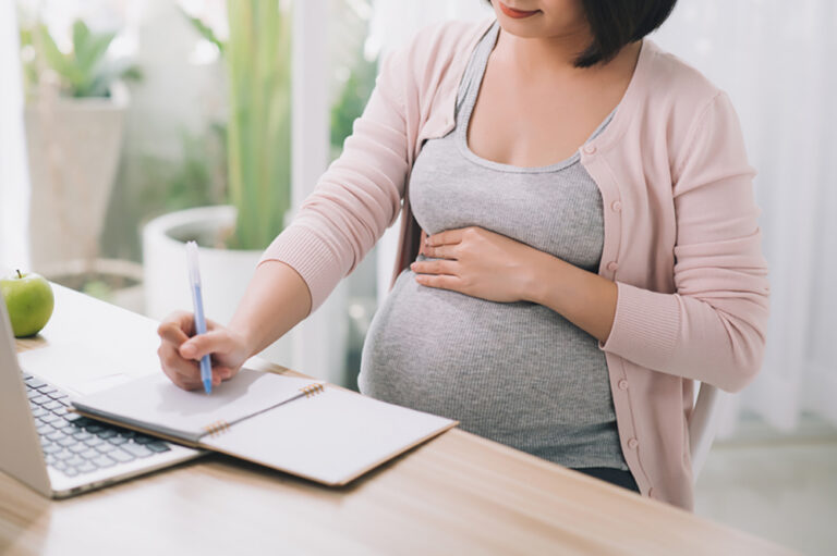 pregnant woman sits by a desk in an office